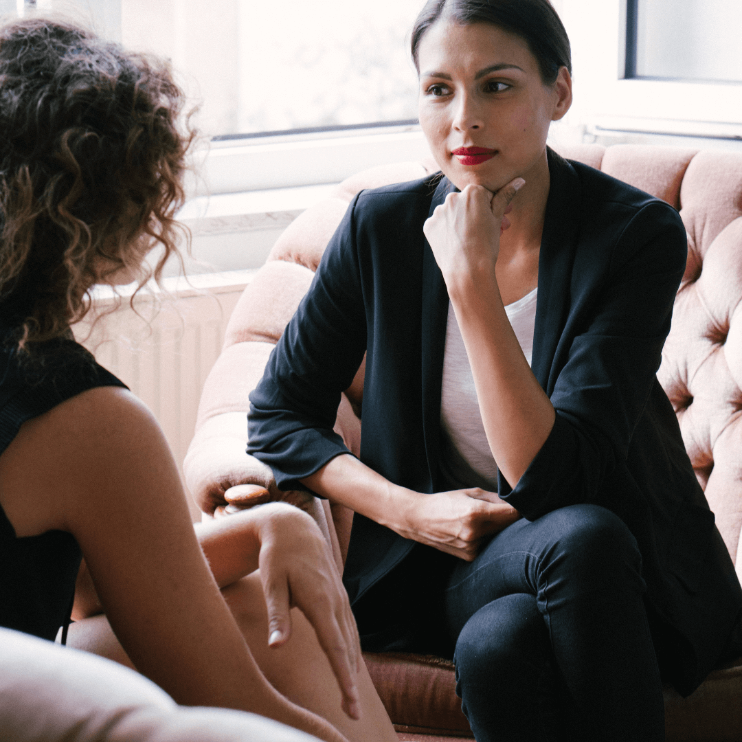 Femme assise sur un canapé qui se tient la tête en écoutant une autre personne