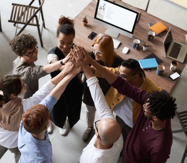 L'engagement-collectif 8 personnes qui réunissent leurs mains en l'air avec un bureau en fond