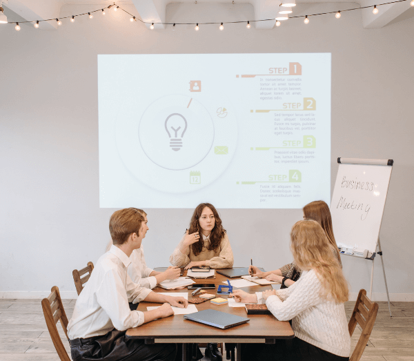 4 personnes autour d'une table qui discutent au travail avec une image projetée au fond