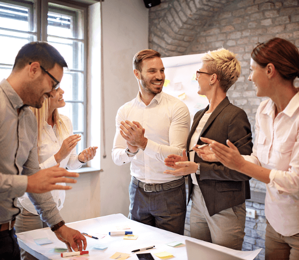 Groupe de 5 personnes qui applaudissent autour d'une table au travail