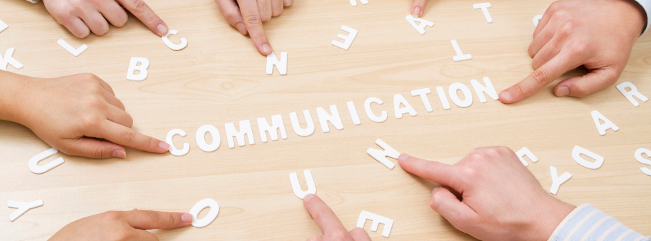 Plusieurs mains qui montre du doigt des lettres posés sur une table avec écrit "communication"